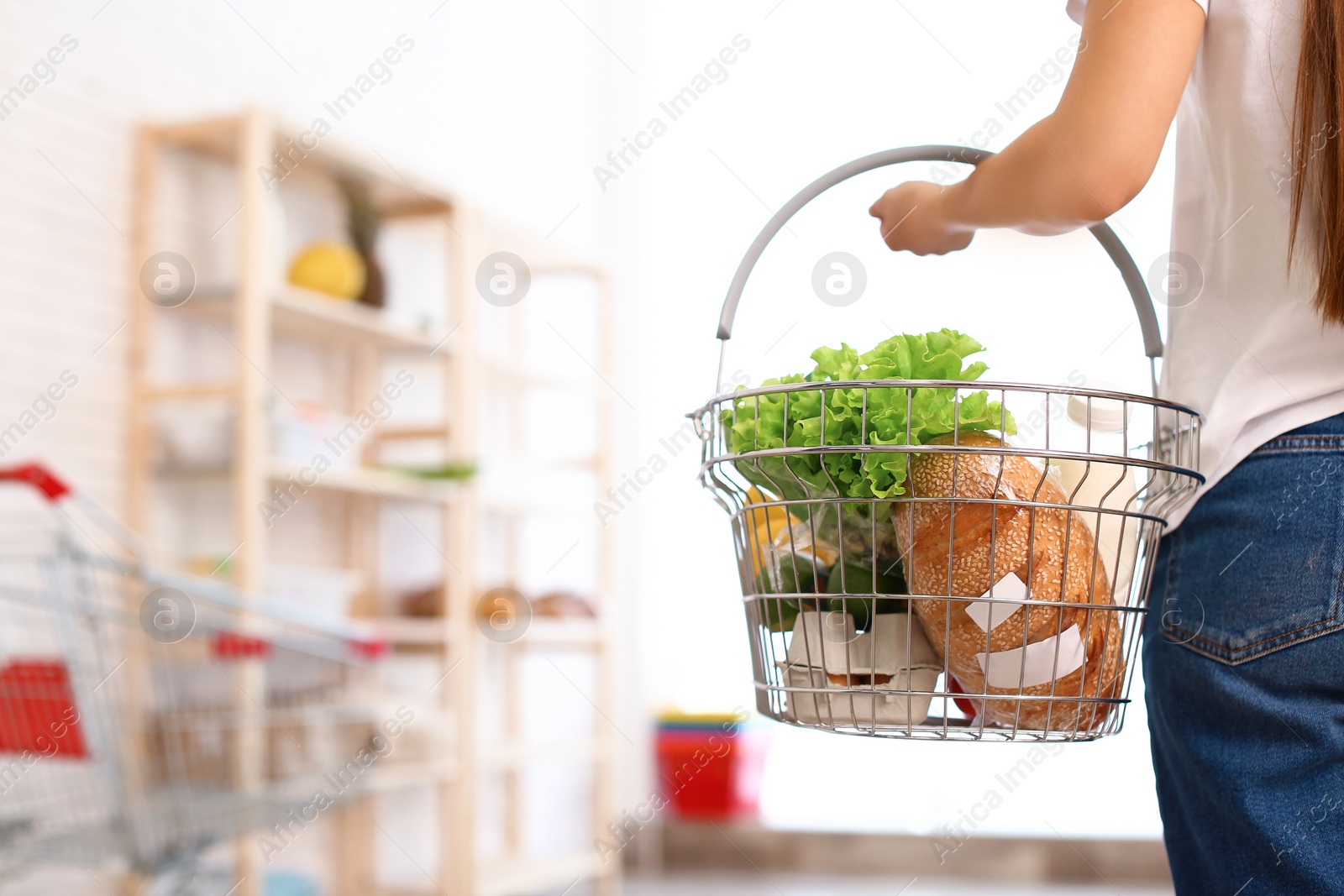 Photo of Woman with shopping basket full of products in grocery store, closeup