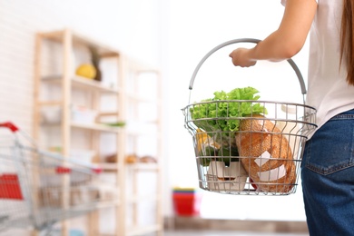 Woman with shopping basket full of products in grocery store, closeup