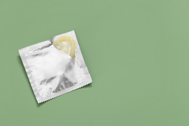 Photo of Condom in torn package on light green background, top view with space for text. Safe sex