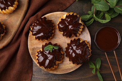 Delicious profiteroles with chocolate spread and mint on wooden table, flat lay