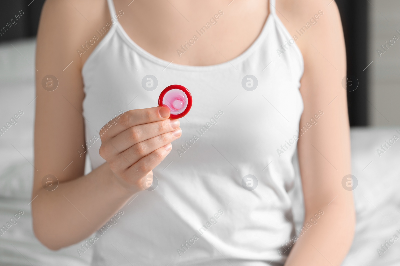 Photo of Woman holding unpacked condom on blurred background, closeup. Safe sex