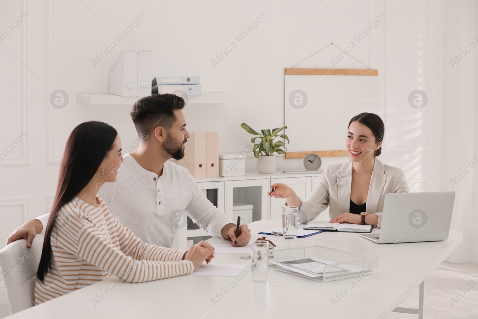 Photo of Happy young couple signing purchase contract in real estate agent's office. Mortgage concept