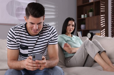 Internet addiction. Man with smartphone ignoring his girlfriend in living room