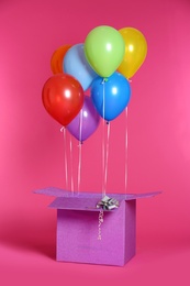 Gift box with bright air balloons on color background