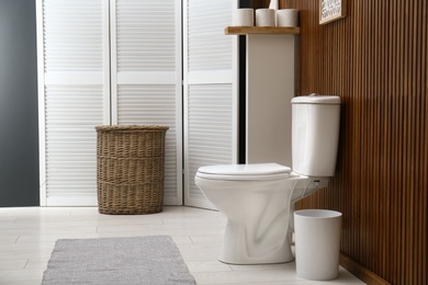 Photo of White toilet bowl near wooden wall in modern bathroom interior