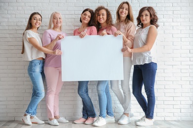 Photo of Women wearing silk ribbons holding poster with space for text against brick wall. Breast cancer awareness concept