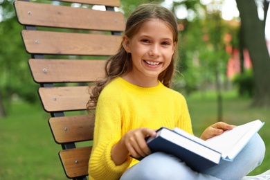 Happy little girl reading book in park 