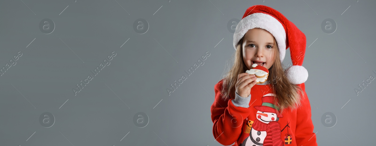 Image of Cute little girl with Christmas gingerbread cookie on grey background, space for text. Banner design