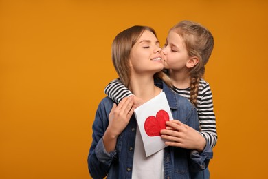 Photo of Little daughter congratulating her mom with postcard on orange background, space for text. Happy Mother's Day