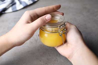 Woman holding glass jar of Ghee butter over grey table, closeup