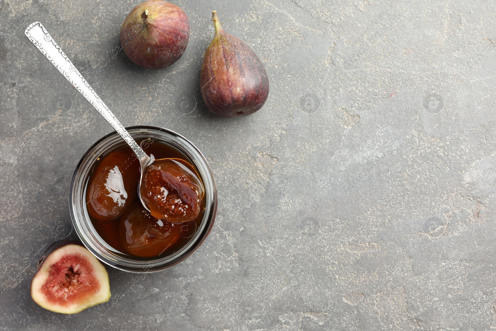 Photo of Jar of tasty sweet jam and fresh figs on grey table, flat lay. Space for text