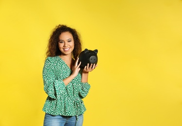 Photo of Young African-American woman with piggy bank on color background, space for text. Money saving