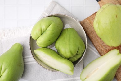 Photo of Cut and whole chayote in bowl on white tiled table, flat lay