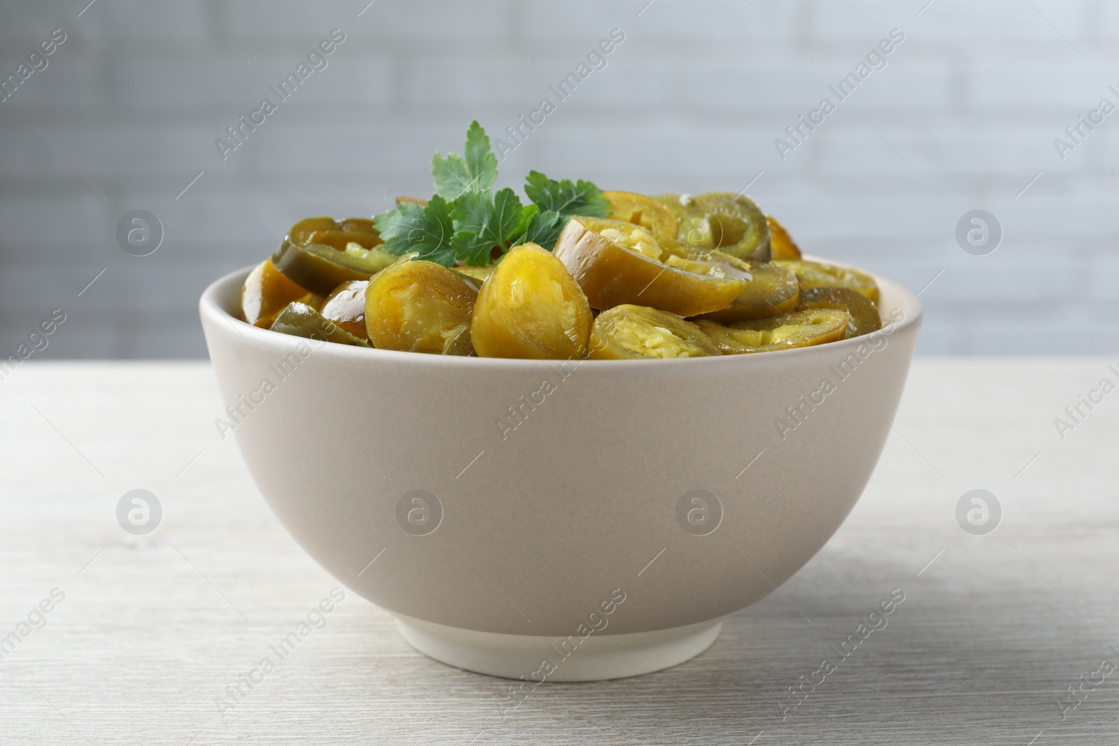 Photo of Bowl with slices of pickled green jalapeno peppers on white wooden table