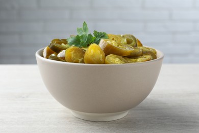 Photo of Bowl with slices of pickled green jalapeno peppers on white wooden table