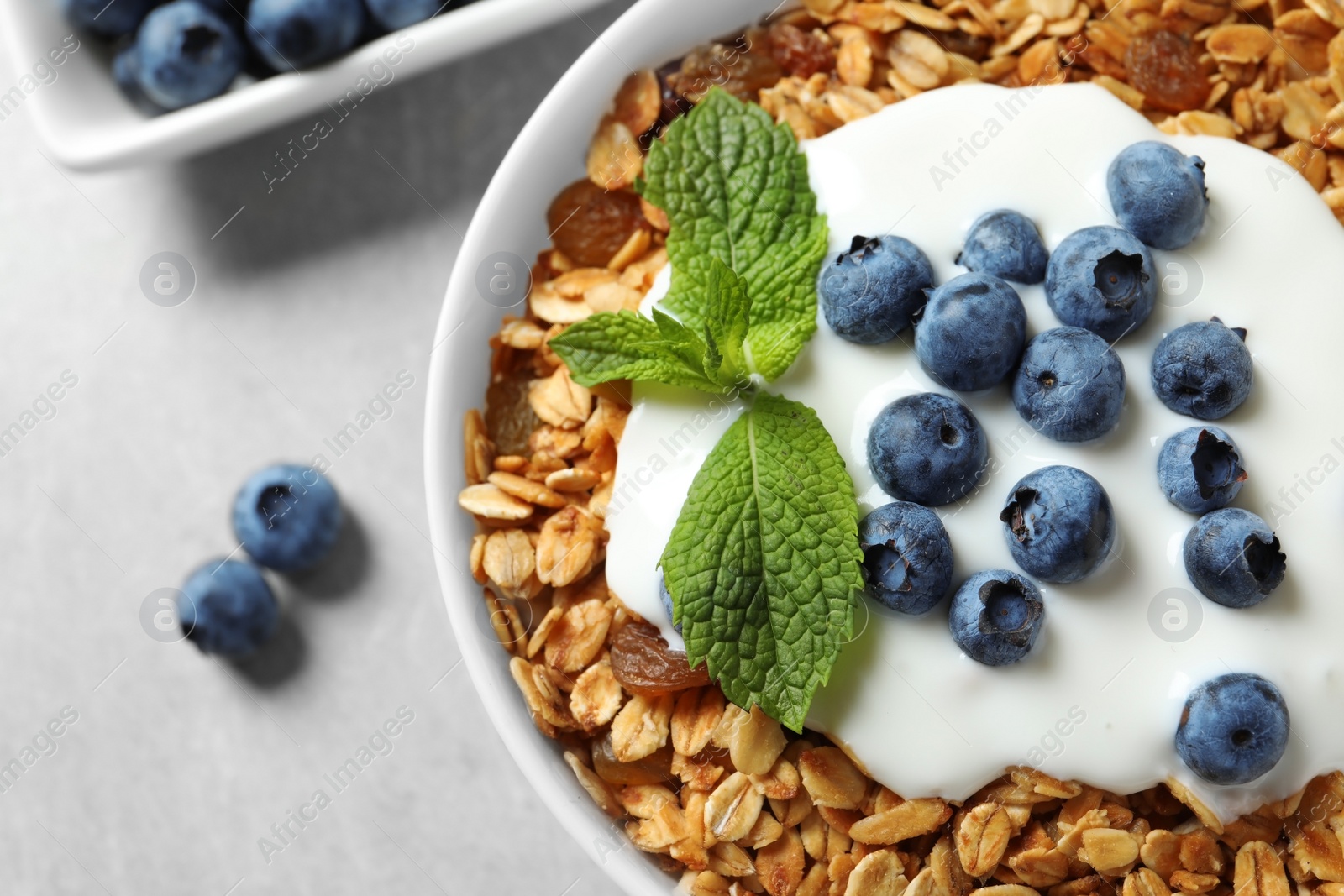 Photo of Delicious yogurt with granola and blueberries in bowl on grey table, top view