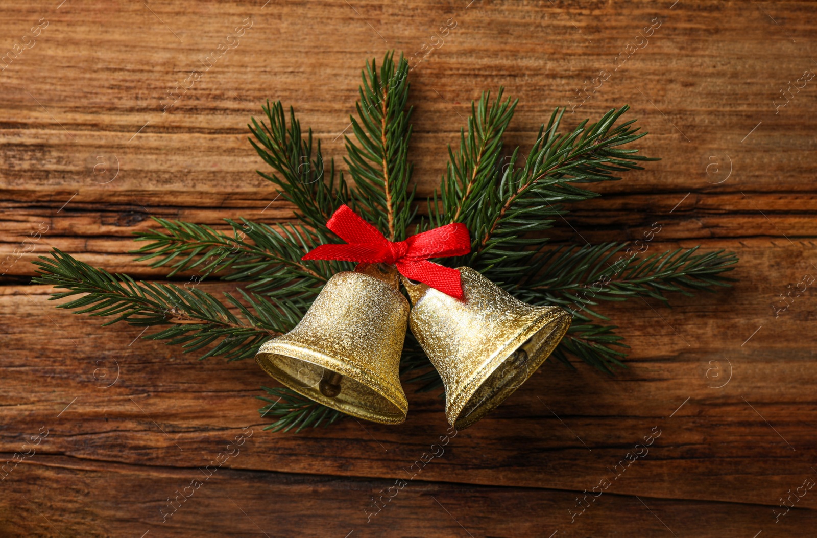 Photo of Christmas bells and fir tree branches on wooden table, flat lay