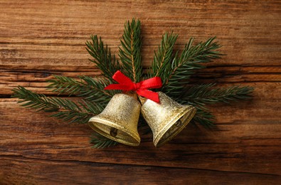 Photo of Christmas bells and fir tree branches on wooden table, flat lay