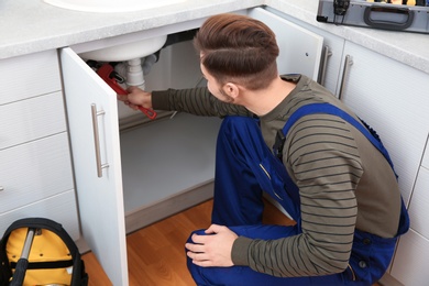 Male plumber in uniform repairing kitchen sink