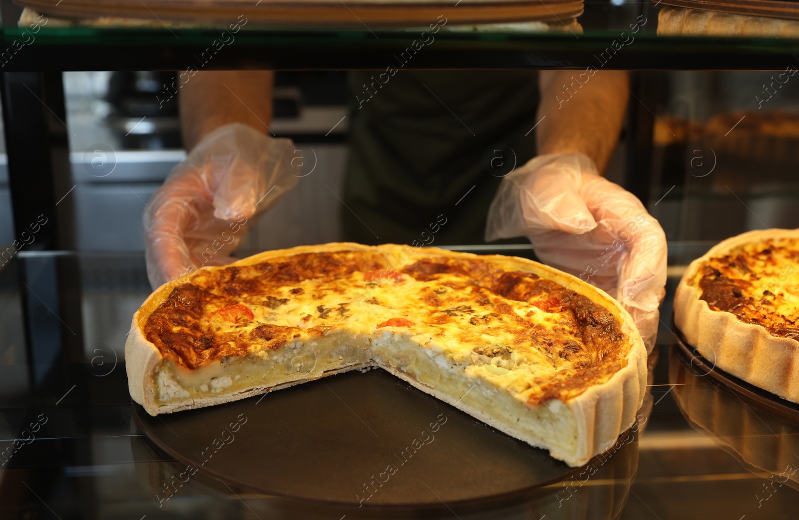 Photo of Seller taking tasty quiche from showcase in bakery shop, closeup