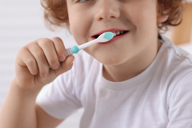 Photo of Little boy brushing his teeth with plastic toothbrush on blurred background, closeup