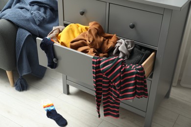 Photo of Cluttered chest of drawers indoors. Clothes in mess