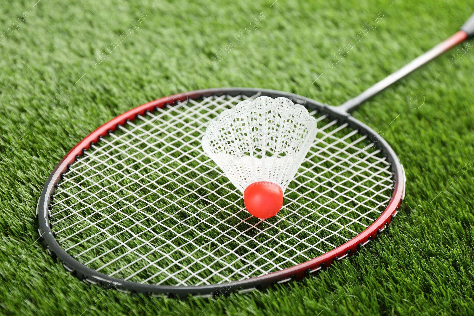 Photo of Badminton racket and shuttlecock on green grass outdoors, closeup