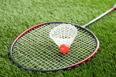 Photo of Badminton racket and shuttlecock on green grass outdoors, closeup