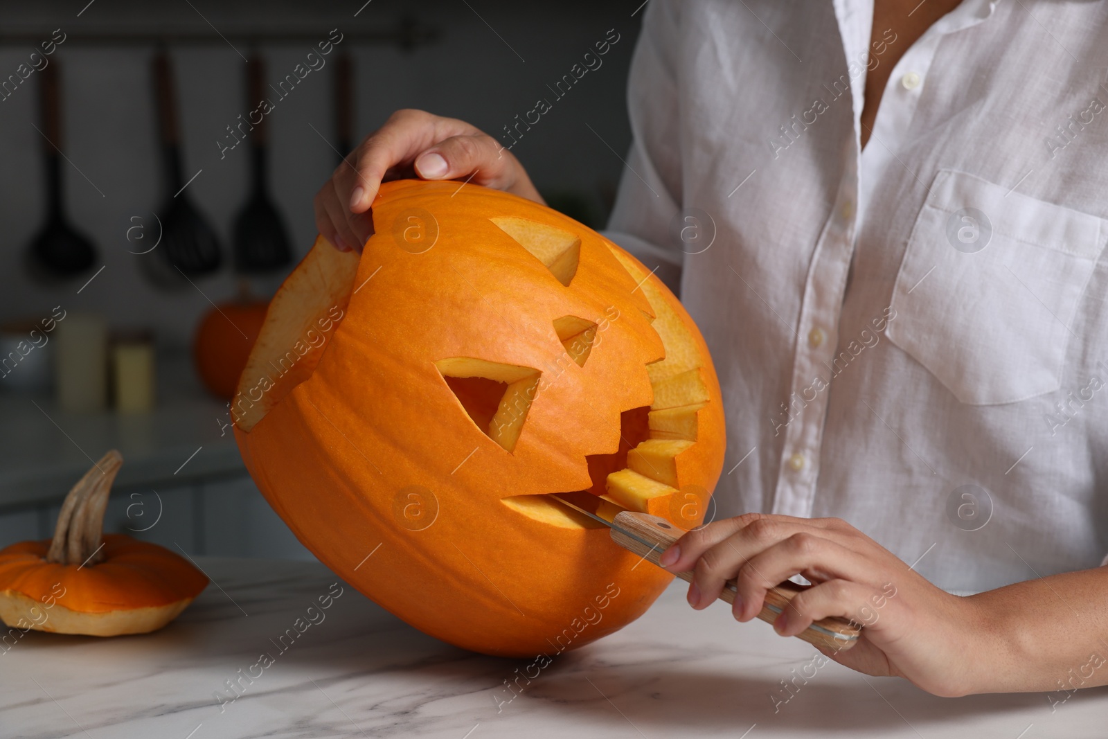 Photo of Woman carving pumpkin for Halloween at white marble table in kitchen, closeup