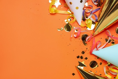 Party hats, glitter and streamers on orange background, flat lay. Space for text