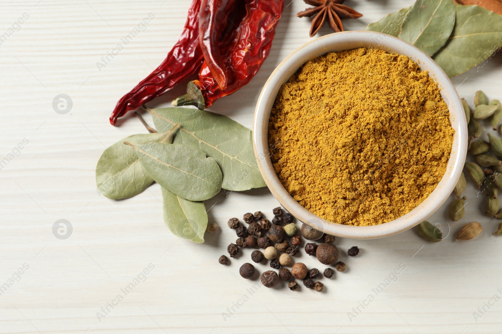 Photo of Curry powder in bowl and other spices on white wooden table, flat lay. Space for text