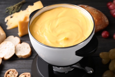 Pot with delicious cheese fondue on wooden table