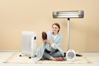 Photo of Young woman with different modern electric heaters near beige wall indoors