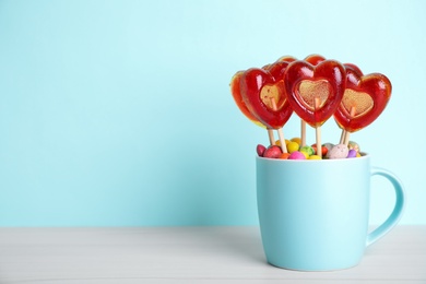 Delicious heart shaped lollipops and dragees on table against light blue background. Space for text