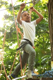 Little African-American boy climbing in adventure park. Summer camp