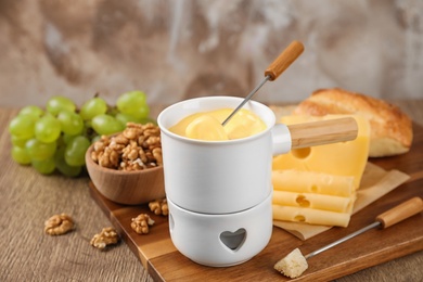 Pot of tasty cheese fondue and fork with bread on wooden table