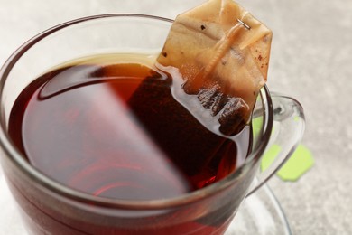 Photo of Brewing tea. Glass cup with tea bag on table, closeup