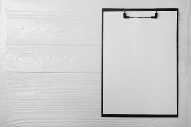 Photo of New clipboard with sheet of blank paper on white wooden table, top view. Space for text