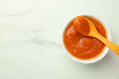 Bowl with healthy baby food and spoon on white marble table, top view. Space for text