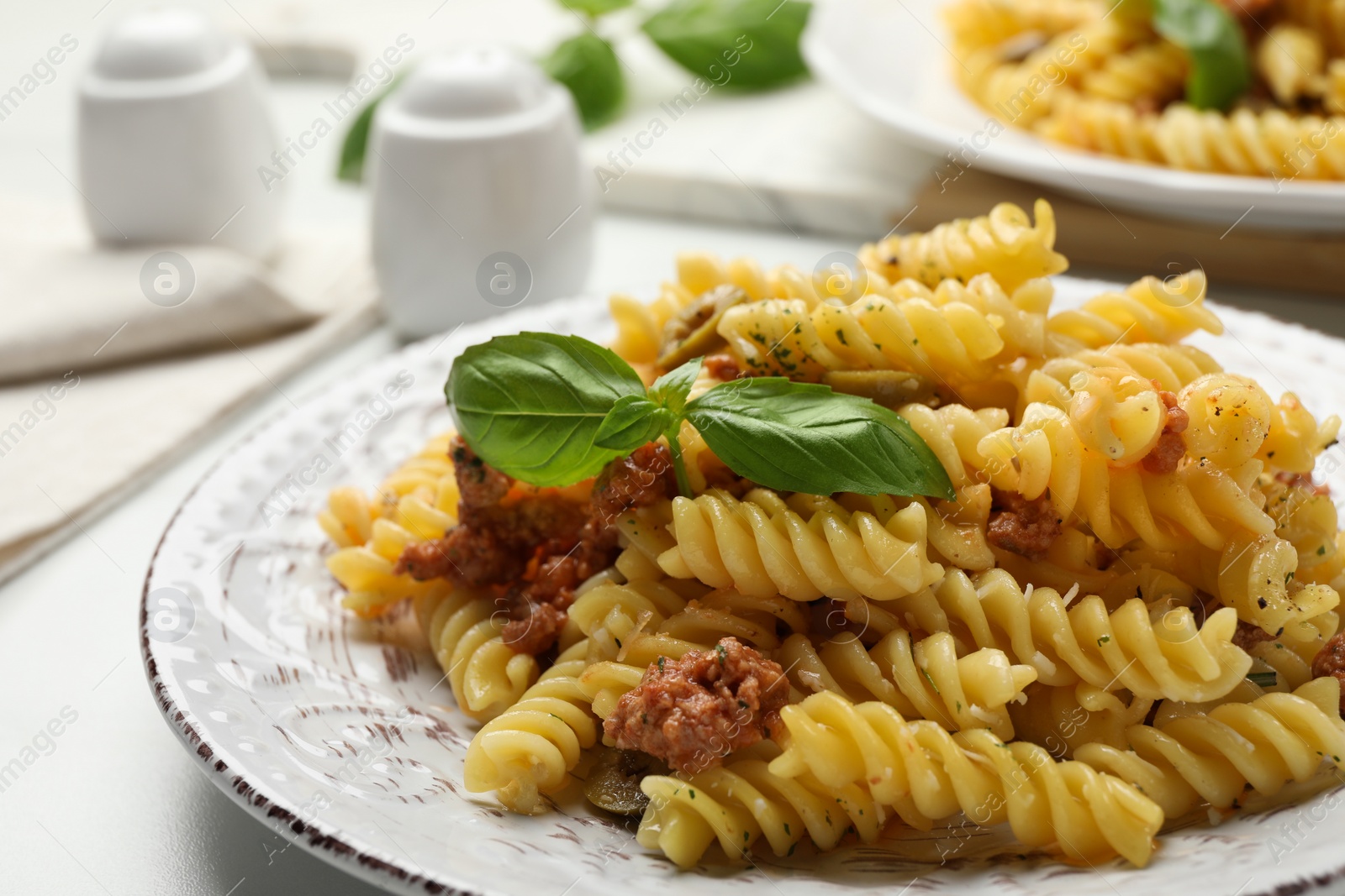 Photo of Plate of delicious pasta with minced meat and basil on white table, closeup