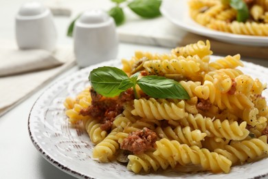 Plate of delicious pasta with minced meat and basil on white table, closeup
