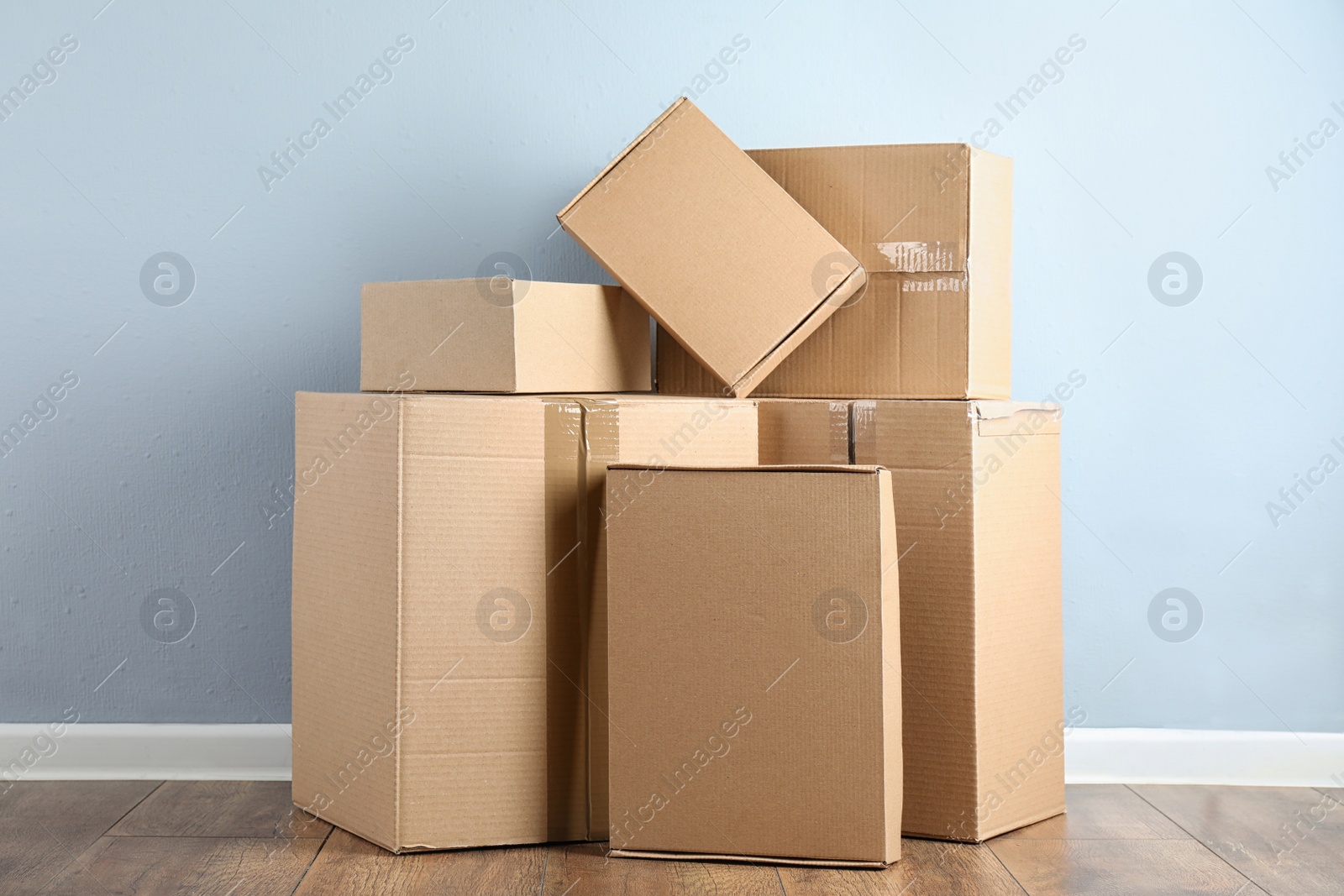 Photo of Pile of cardboard boxes near light blue wall indoors