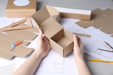 Woman creating packaging design at light wooden table, closeup