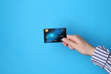 Woman holding credit card on light blue background, closeup