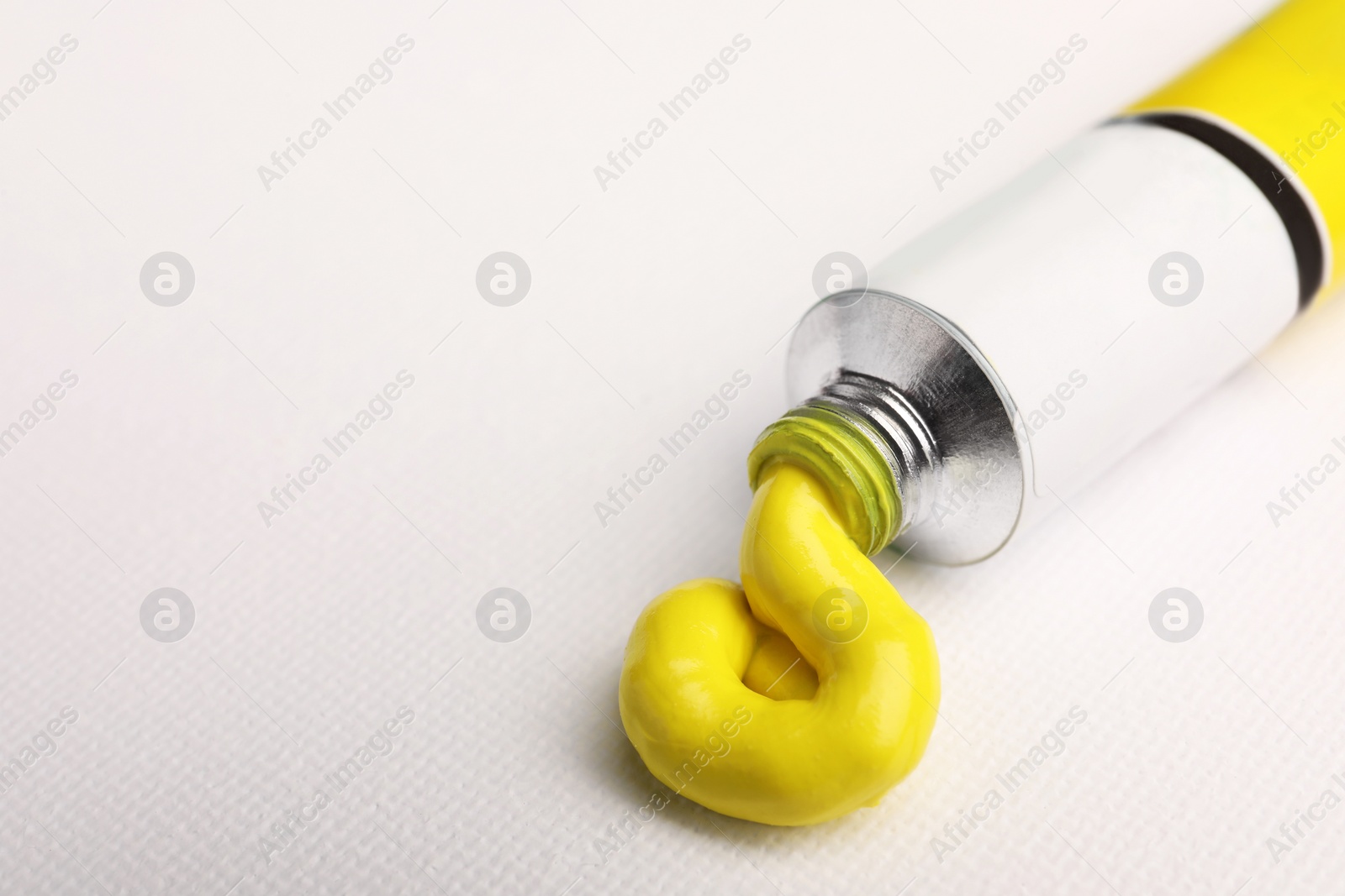 Photo of Tube with yellow oil paint on blank canvas, closeup. Space for text