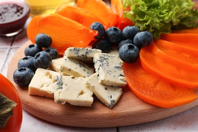 Delicious persimmon, blue cheese and blueberries on table, closeup