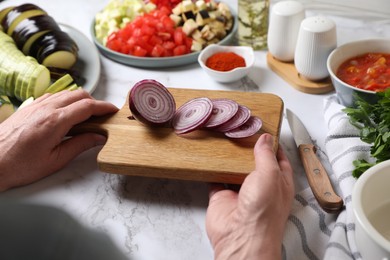 Cooking delicious ratatouille. Woman holding board with cut fresh onion at white marble table, closeup