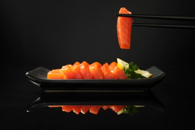 Photo of Taking delicious piece of salmon from serving board on black mirror surface. Tasty sashimi dish