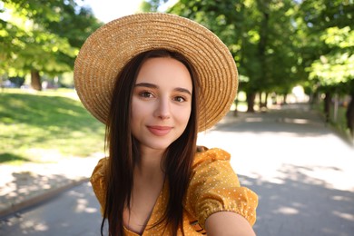 Photo of Travel blogger in straw hat takIng selfie outdoors