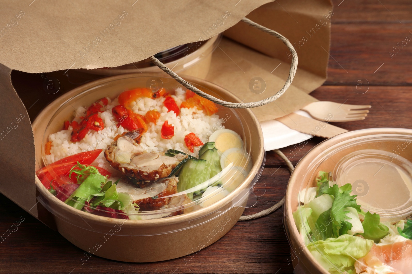Photo of Tasty food in containers with knife and fork on wooden table